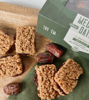 A close up photo of Gluten Free Date Bars on a wooden platter with a green napkin with scattered Medjool Dates and a box of Medjool Dates in the corner. 