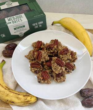 A picture of a plate of Banana Date Drops with a box of Medjool dates at the top and bananas and dates scattered