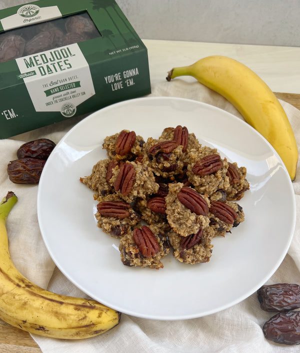A picture of a plate of Banana Date Drops with a box of Medjool dates at the top and bananas and dates scattered